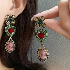 Vintage style gold earrings featuring a red crystal heart and elegant pink cameo relief detail