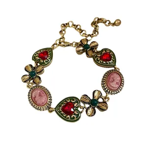 Ornate vintage gold-tone necklace featuring red heart crystals, floral charms, and pink cameos.