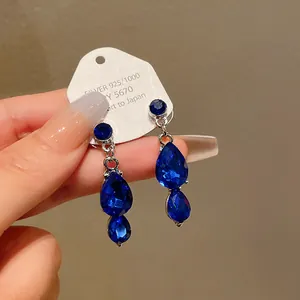Close-up of elegant blue teardrop crystal earrings with silver setting on a display card