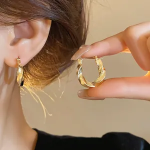 Détail des boucles d'oreilles créoles torsadées dorées portées à l'oreille et à la main