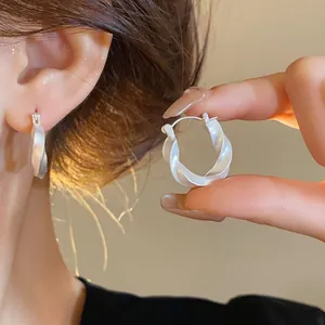 Vue détaillée de près d'élégantes boucles d'oreilles créoles torsadées argentées en main