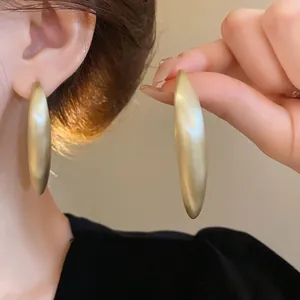 Vue rapprochée de boucles d'oreilles créoles dorées mates à la finition texturée.