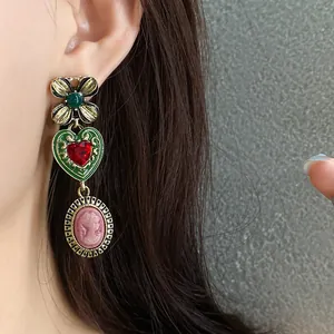 Vintage dangling earrings featuring a green flower, red heart, and pink cameo portrait.