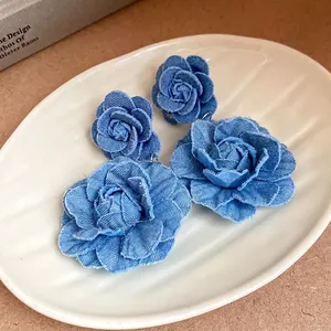 Fashionable blue denim fabric flower earrings for women on a white rippled ceramic plate