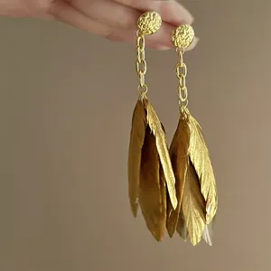 Detailed view of elegant golden Bohemian feather drop earrings featuring hammered metal studs