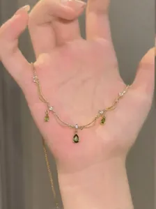 Vue détaillée d'un collier plaqué or 18k avec pendentifs gouttes d'eau vertes dans la main.