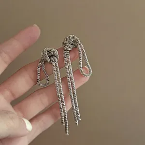 Close-up of vintage silver mesh chain knot tassel earrings held by hand to show texture.
