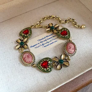Vintage gold necklace featuring red hearts, green flowers, and pink cameos in a box.