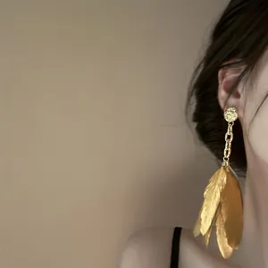 Detailed view of long gold feather earrings worn on ear, showcasing a bohemian style