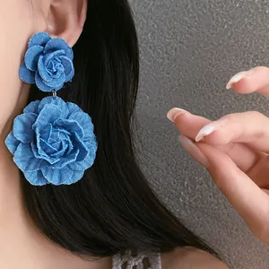 Detailed close-up of handmade blue denim fabric rose flower earrings with layers