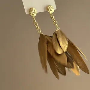 Macro detail of bohemian vintage style long brown feather tassel earrings with golden studs.