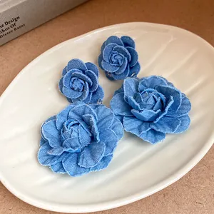 Detailed macro view of blue denim fabric rose flower earrings on a white plate
