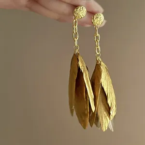 Detailed view of elegant golden feather drop earrings with textured round studs.