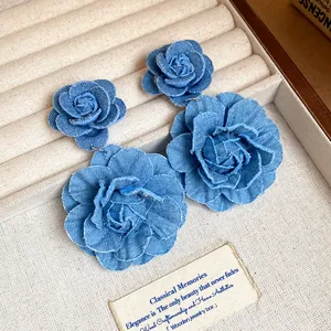 Detailed macro view of blue denim fabric rose earrings resting in a beige jewelry box