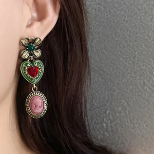 Elegant vintage-inspired drop earrings featuring a green heart and pink cameo portrait.