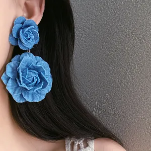Detailed macro shot of large blue denim fabric rose flower earrings on model's ear
