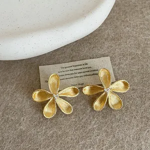 Macro view showing the detailed brushed gold texture of these flower stud earrings