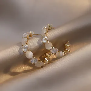Macro view of gold plated C-shaped hoop earrings with alternating white stones and CZ crystals.