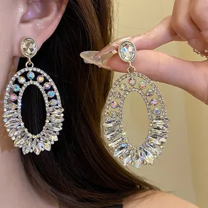 Close-up detail of luxurious silver needle oval pendant earrings with inlaid crystals.