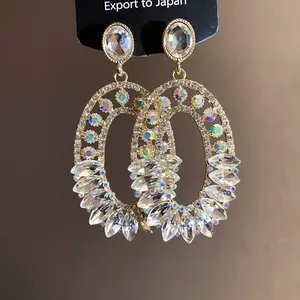 Close-up detail of ornate gold-tone oval drop earrings featuring shimmering iridescent crystals.