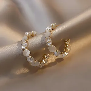 Detailed view of C-shaped gold hoop earrings with white stones and crystals on satin.