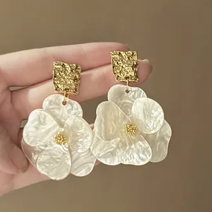 Primo piano di orecchini a fiore eleganti con parte superiore dorata e petali madreperla