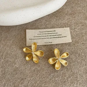 Close-up of French minimalist gold flower stud earrings with a matte brushed texture.