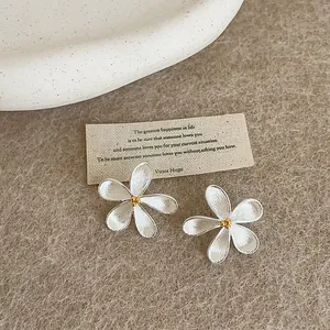 Close-up of French minimalist silver flower earrings with gold centers on a beige background.