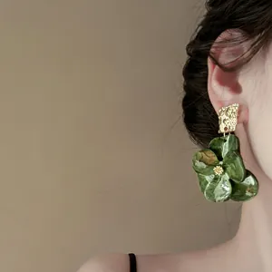 Primo piano di eleganti orecchini a fiore verde con perno dorato testurizzato su modella.