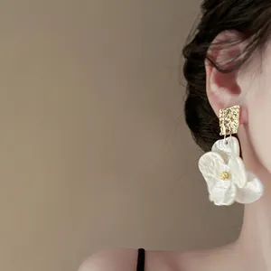Dettaglio di eleganti orecchini a fiore bianco con borchie geometriche irregolari oro.