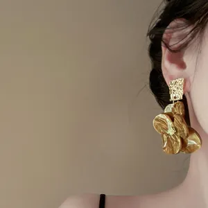 Dettaglio degli orecchini pendenti a fiore ambrati e metallo dorato martellato su una modella