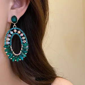 Detailed close-up of vintage emerald green rhinestone oval dangling earrings with silver needles