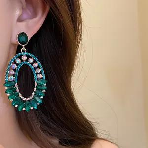 Close-up of emerald green oval dangle earrings with shimmering rhinestones on ear.