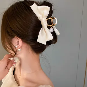 Primo piano di un fermaglio per capelli a fiocco in raso bianco crema con perla