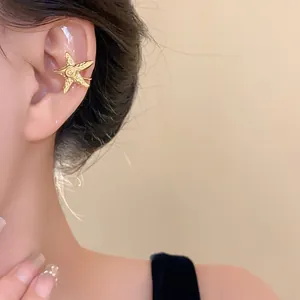 Detailed close-up shot of a minimalist gold metal starfish ear cuff worn on an ear