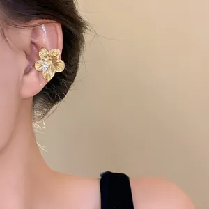 Detail view of an elegant gold flower ear cuff on a model's ear, luxury minimalist style.
