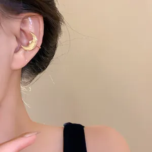 Detailed view of a gold-toned crescent moon ear cuff featuring a carved face design