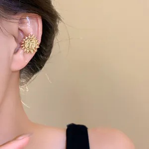 Detail of a gold sun-shaped ear cuff worn on a model's ear, luxury metal jewelry