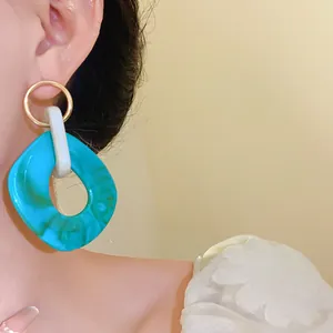Dettaglio di grandi orecchini geometrici in acrilico turchese venato su modella asiatica.