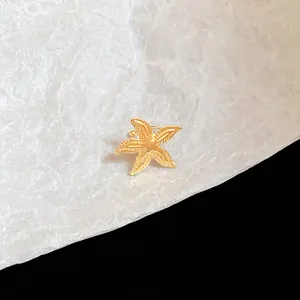 Close-up detail of a textured golden metal starfish ear clip on white background