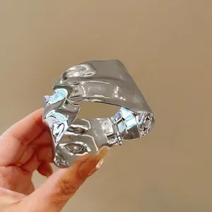 Detailed view of an irregular geometric silver-colored metal cuff bangle held in hand
