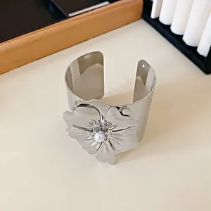 Vista detallada de un brazalete de metal plateado con flor grande y detalle de perla.