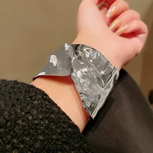 Close-up detail of a silver irregular crumpled metallic cuff bracelet on a model's wrist.