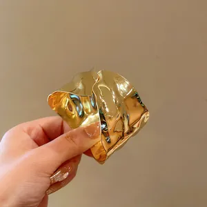 Close-up of a gold irregular wave-shaped metal cuff bracelet with shiny polished finish