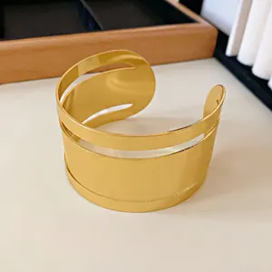 Primer plano de un brazalete ancho dorado con diseño minimalista y líneas caladas.