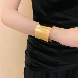 Primer plano de un brazalete ancho de metal dorado con acabado espejo en una modelo