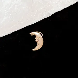 Detail view of a gold-toned crescent moon face ear clip showing metallic texture and design