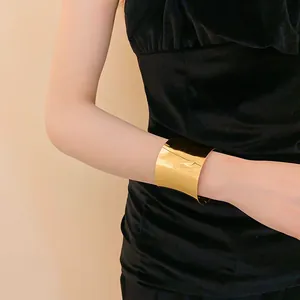 Brazalete ancho dorado minimalista en el brazo de una modelo con vestido negro.