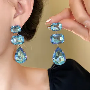 Primo piano di orecchini pendenti con cristalli blu a goccia sull'orecchio della modella