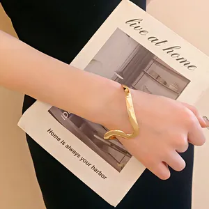 Primer plano detallado de un brazalete dorado ondulado abierto de estilo minimalista